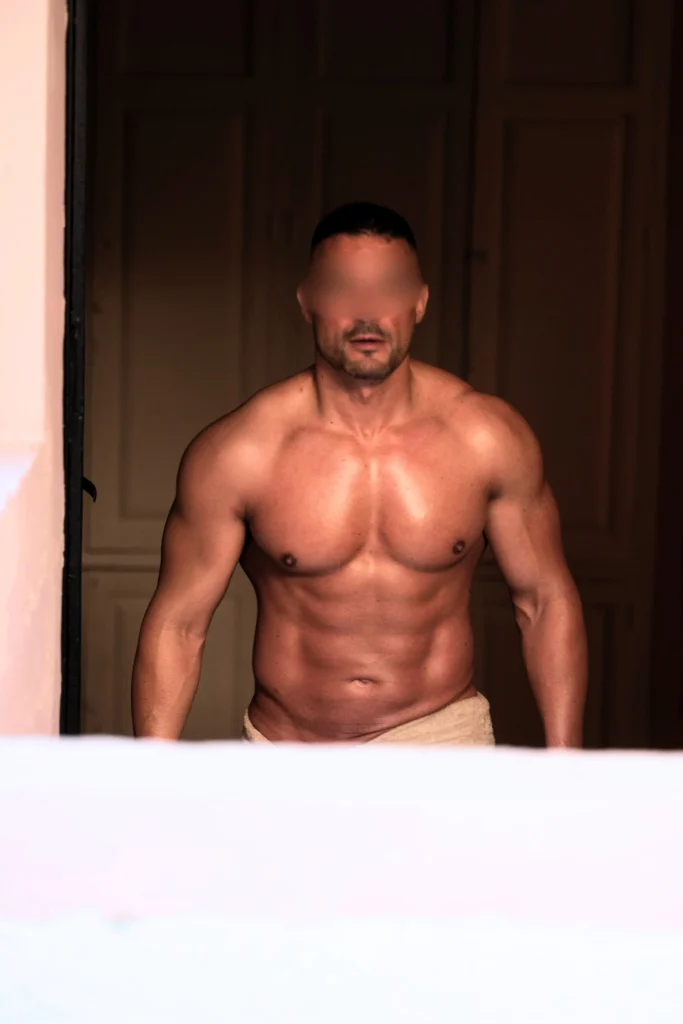 Aleix, masajista de Bliss Barcelona, de pie con el torso definido y cubierto con toalla, posando con seguridad y presencia masculina