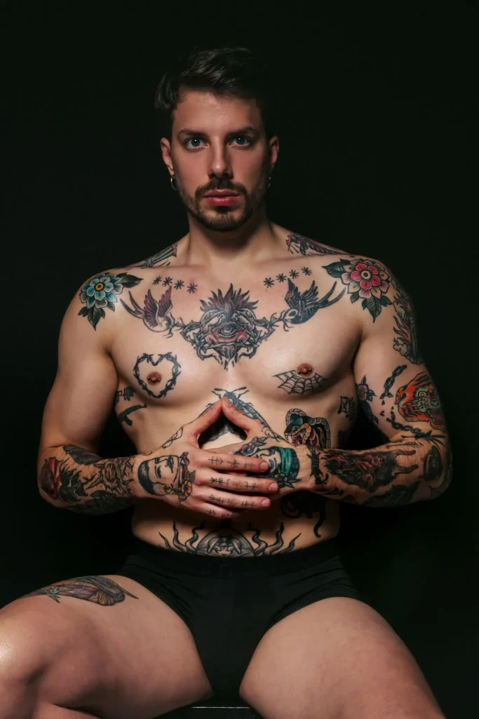 Enea, masajista de Bliss Barcelona, sentado en pose firme mostrando tatuajes en fondo oscuro